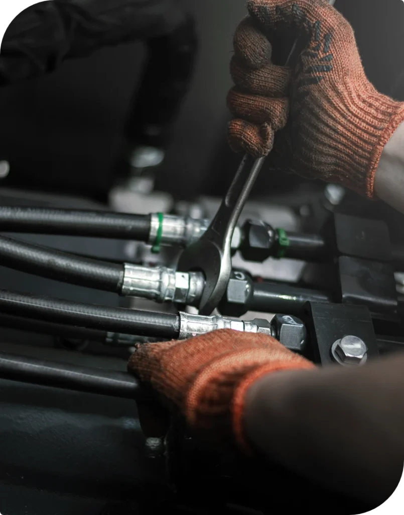Hand i orange arbetshandske drar åt en hydraulkoppling med fast nyckel